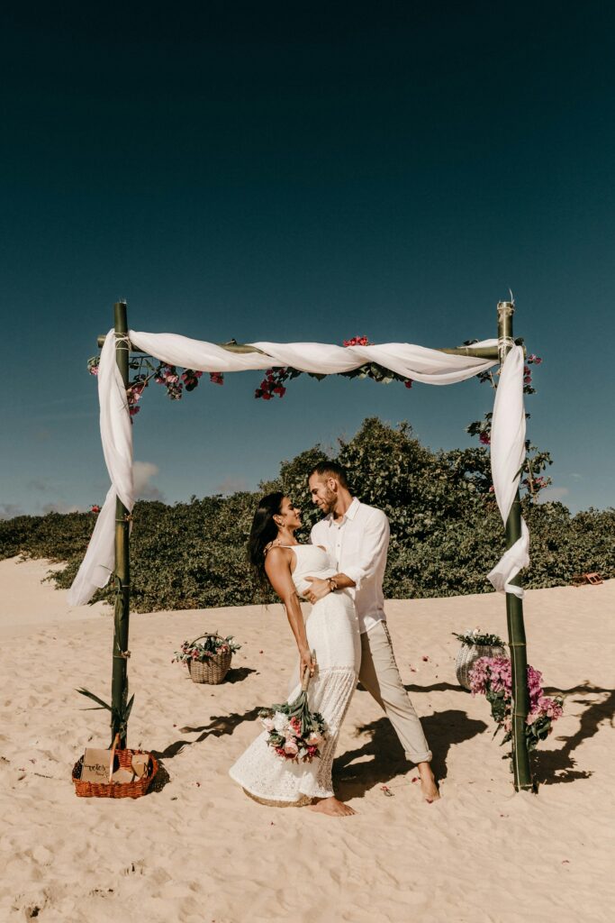 Beach wedding with couple under a decorated bamboo arch, capturing love and romance.