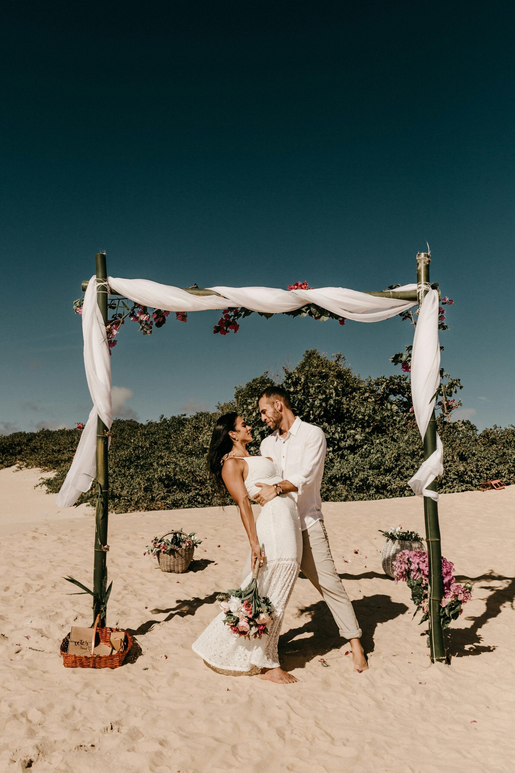 Beach wedding with couple under a decorated bamboo arch, capturing love and romance.
